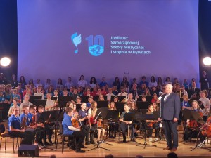 Zdjęcie z koncertu jubileuszowego, przedstawia dziecięcą orkiestrę i chór na scenie